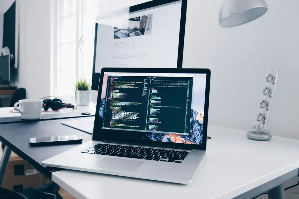 Hands typing on a laptop whose screen shows lines of code.